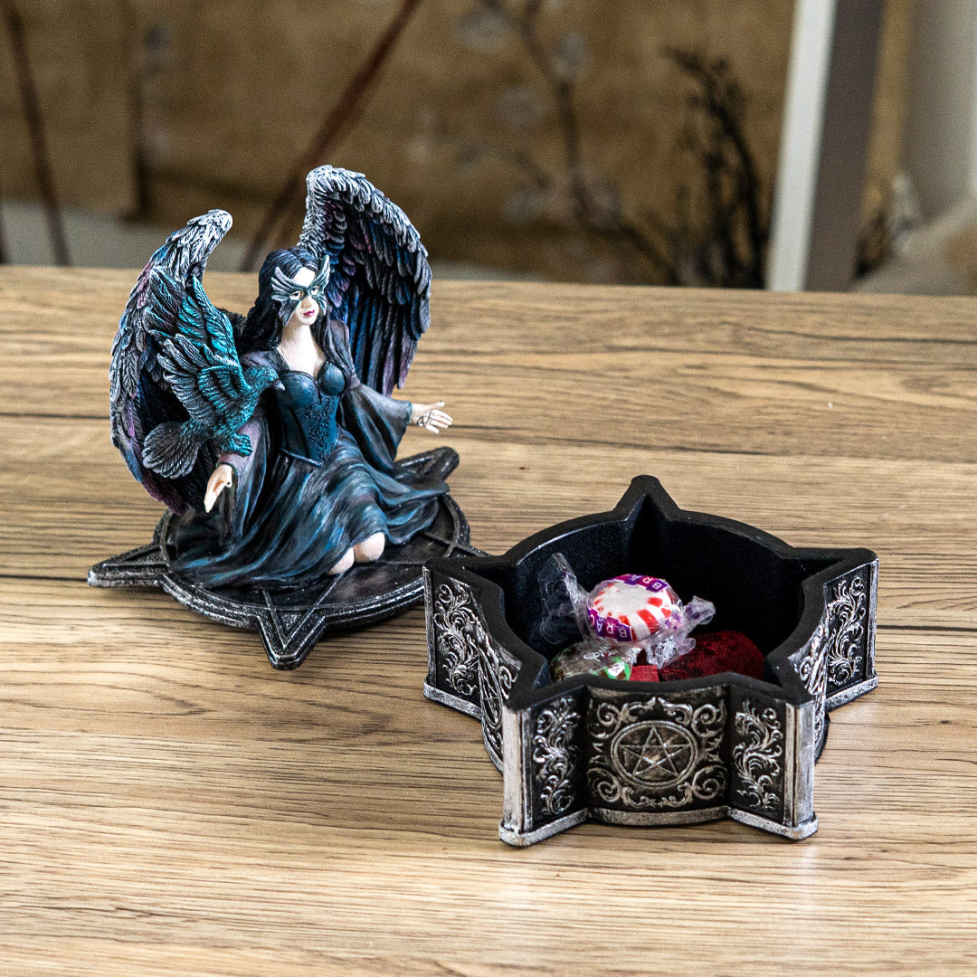 Trinket box, on the lid is a black feather winged angel with a raven on her arm, blue-black dress, black hair, mask. Base of box has pentacle designs, shown open