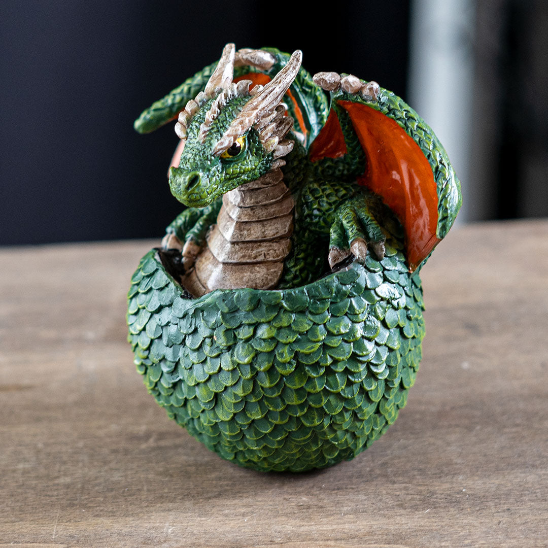 Figurine of a green dragon with red wings and tan belly hatching from an emerald egg with detailed scales