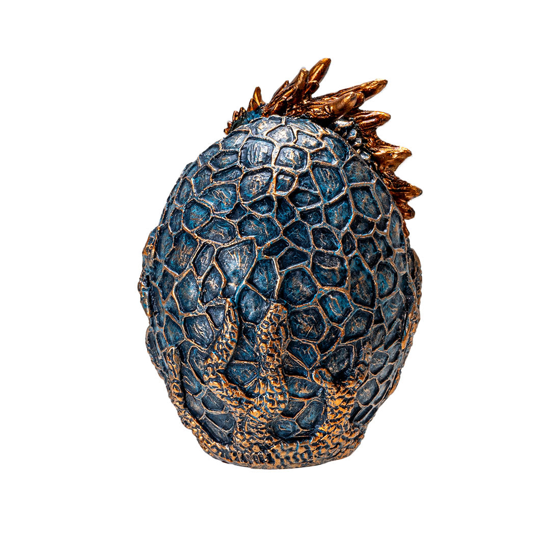 Figurine of a dragon hatching from an egg. Blue textured egg, dragon is indigo with golden accents on horns and spines, shown from the back