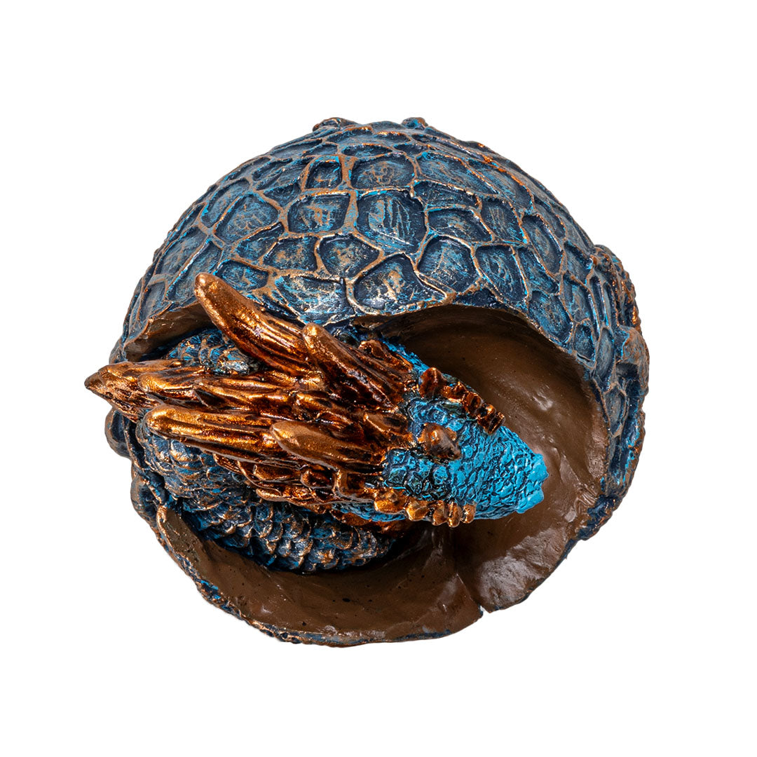 Figurine of a dragon hatching from an egg. Blue textured egg, dragon is indigo with golden accents on horns and spines, shown top down