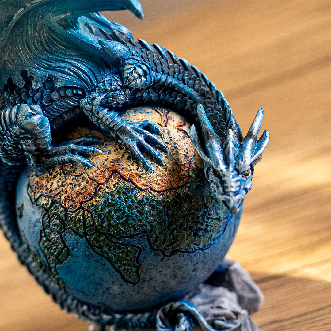 Dragon figurine, perched on planet earth. Blue dragon with tail curled around the globe, close up