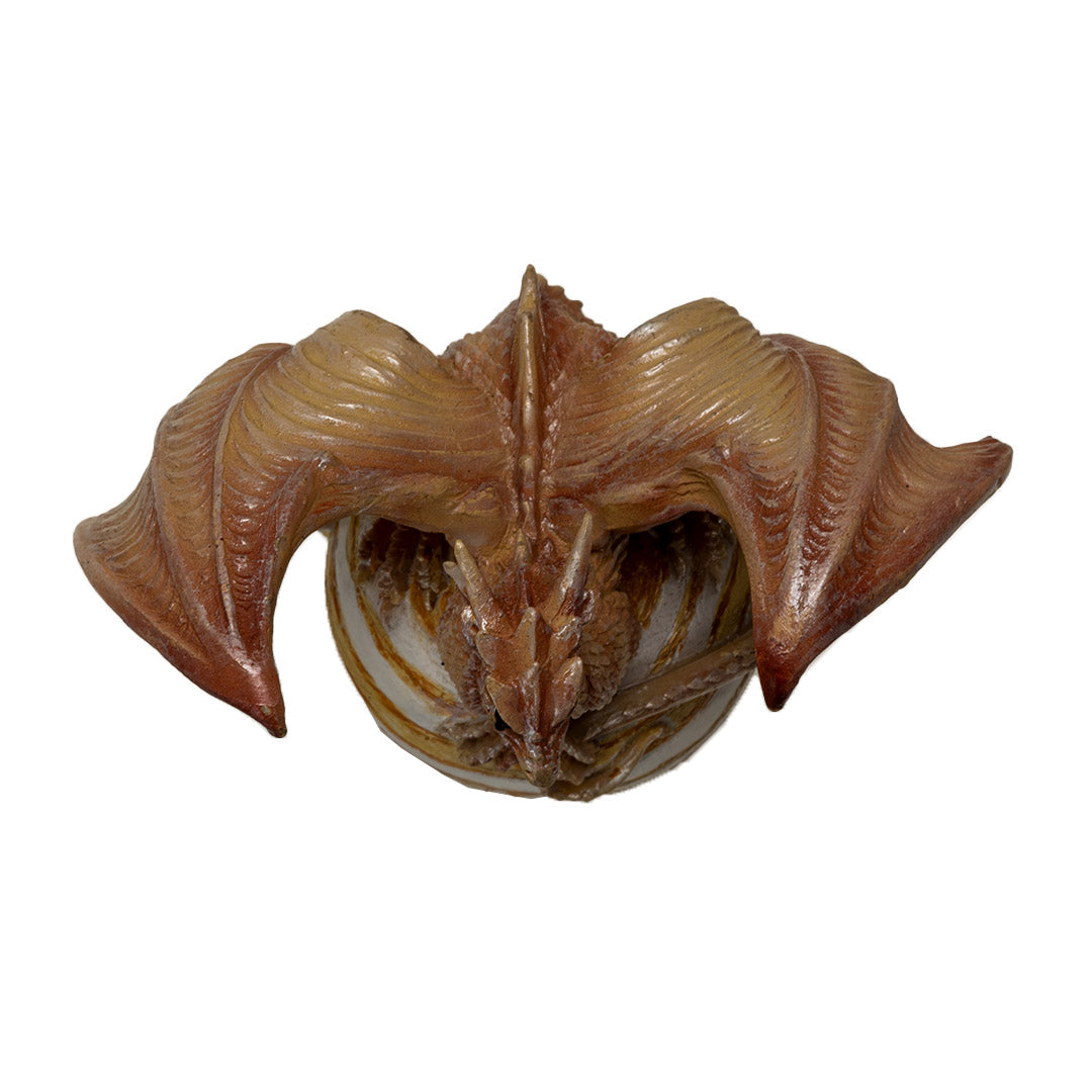 Tan dragon with golden orange eyes perched with crossed talons on the planet Jupiter, striped tan and white on a cloud base, shown top down