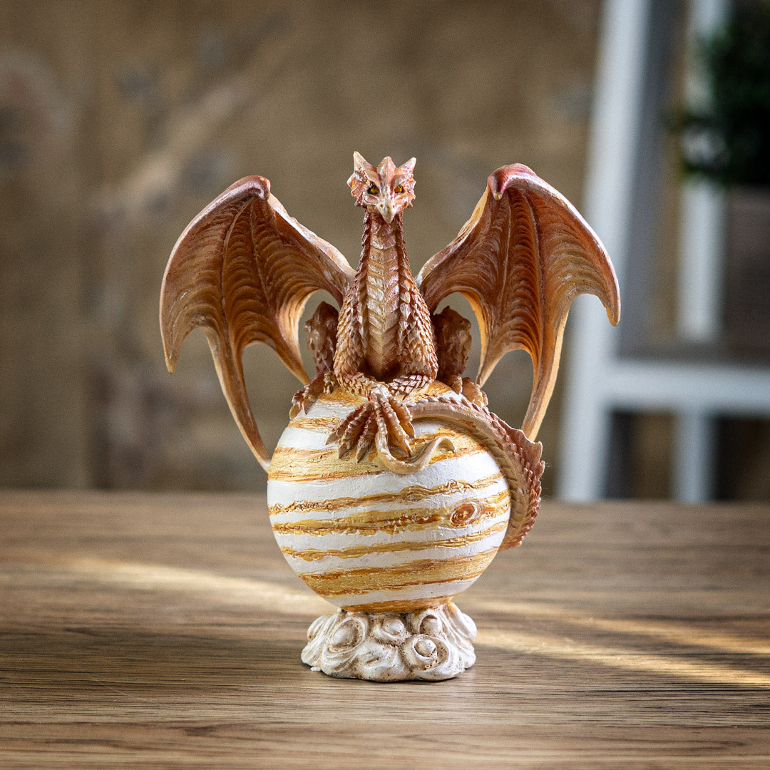 Tan dragon with golden orange eyes perched with crossed talons on the planet Jupiter, striped tan and white on a cloud base