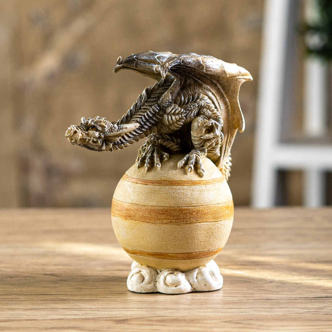 Figurine of a brown dragon perched upon the tan planet Saturn on a cloud base