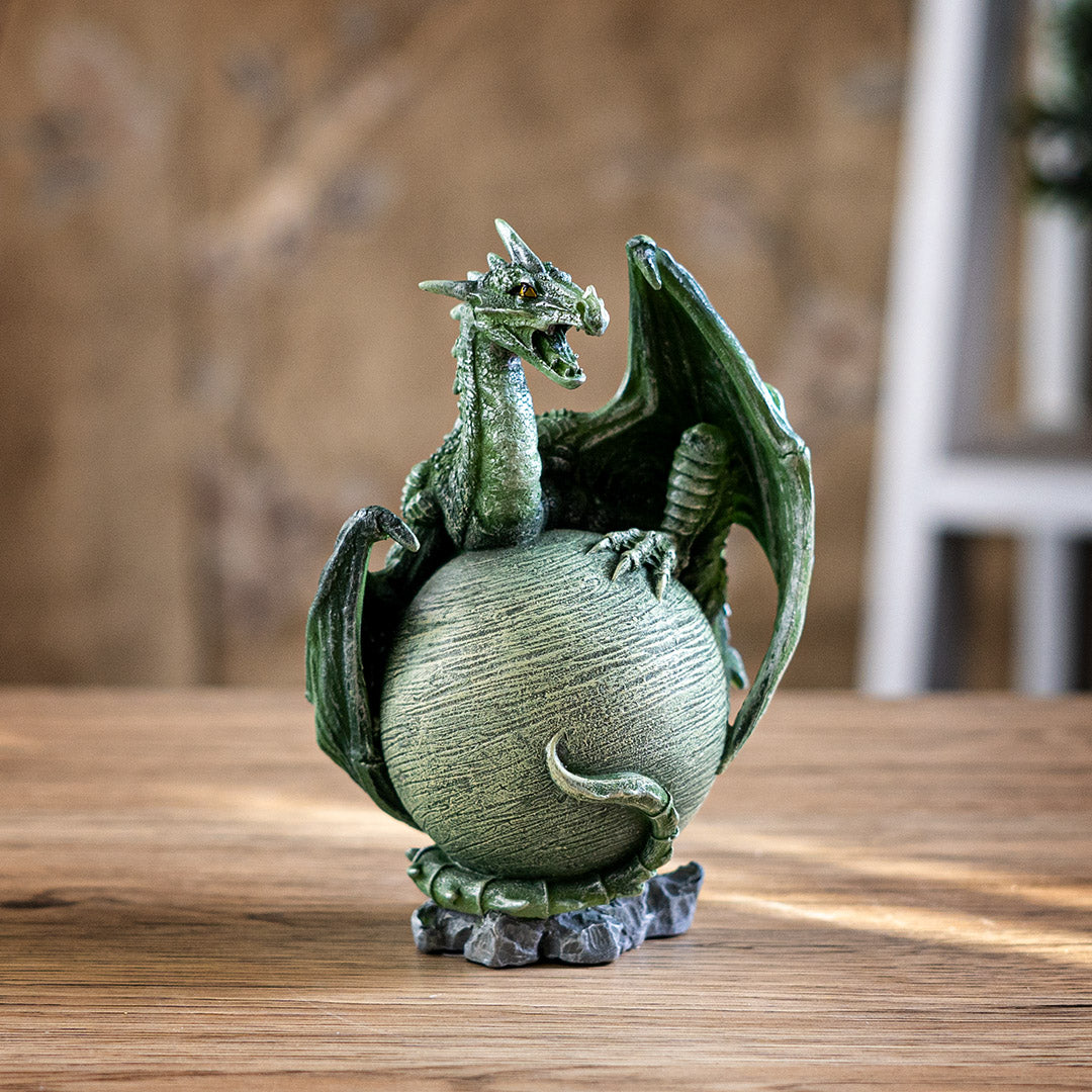 Figurine of a green dragon with open mouth and scorpion tail curled around a light green planet on a rocky base
