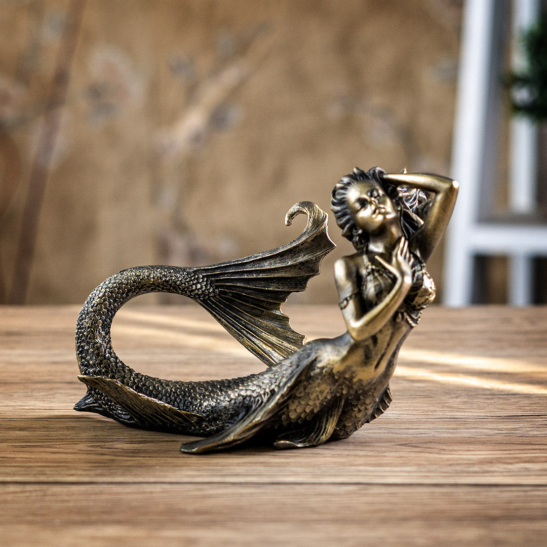 Bronze hued mermaid figurine laying down, with detailed fins and scales, netting top, flowing hair