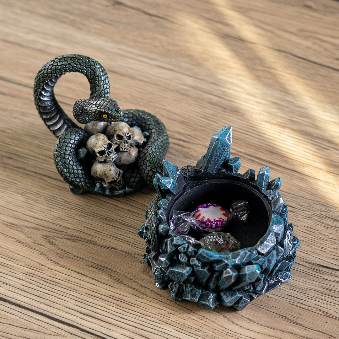 Trinket box, blue crystals on base with yellow-eyed green snake twining through human skull pile, shown open with candy inside