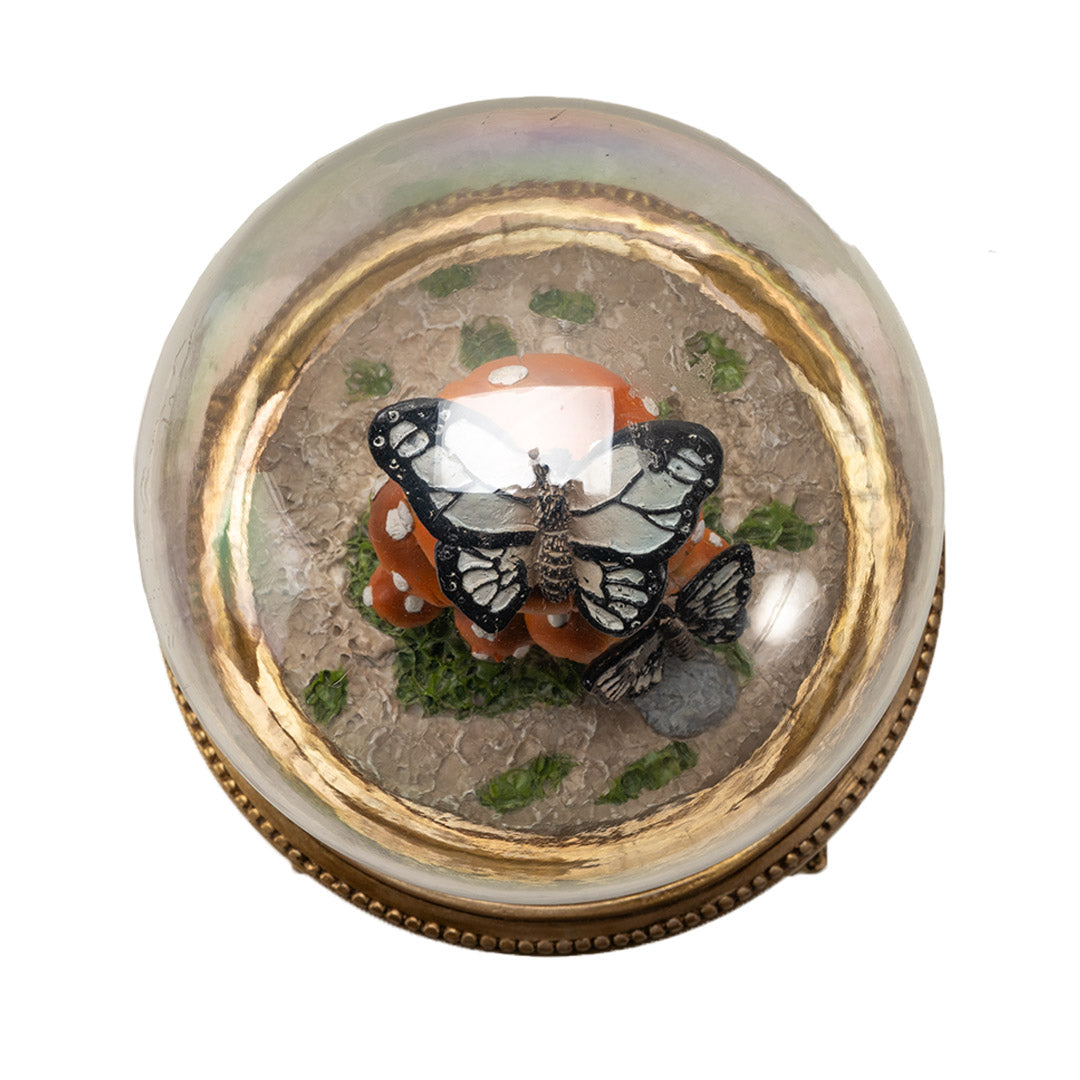 Figurine of butterflies on orange-red mushrooms underneath the glass dome of a cloche, on an ornate golden base, shown top down