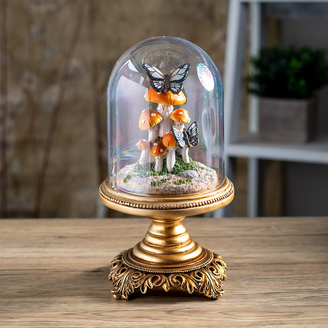 Figurine of butterflies on orange-red mushrooms underneath the glass dome of a cloche, on an ornate golden base