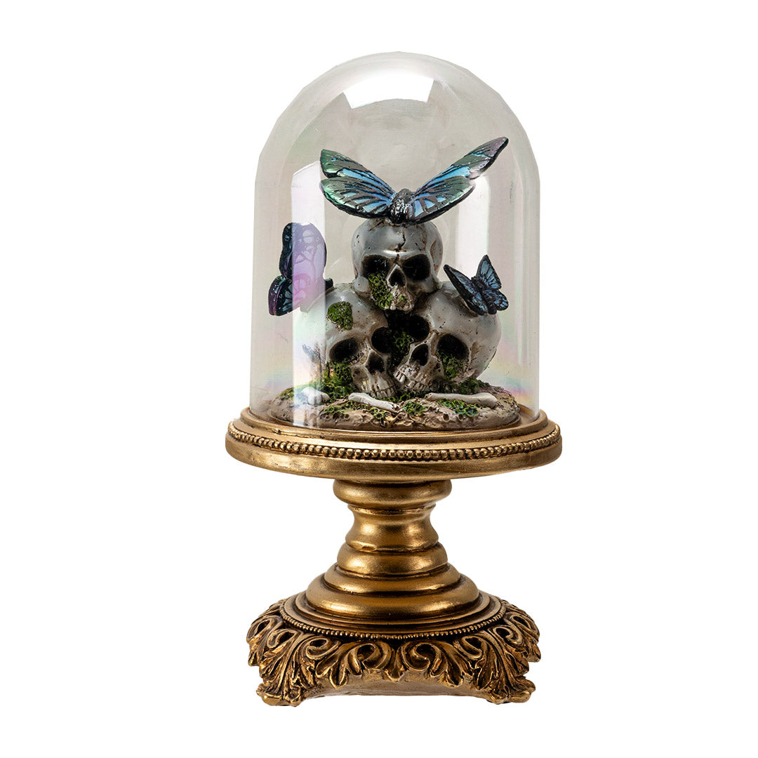 Figurine with three skulls and blue-black butterflies perched on them, moss accents, under a glass cloche dome on an ornate gold base