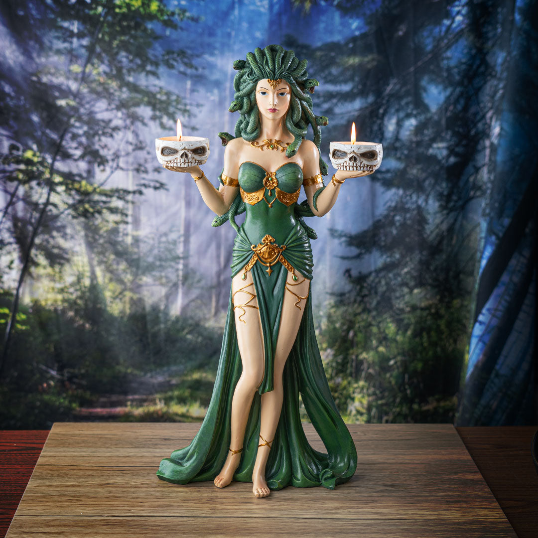 Figurine of Medusa with green snakes for hair, green and gold dress, holding two skull bowls that can hold candles