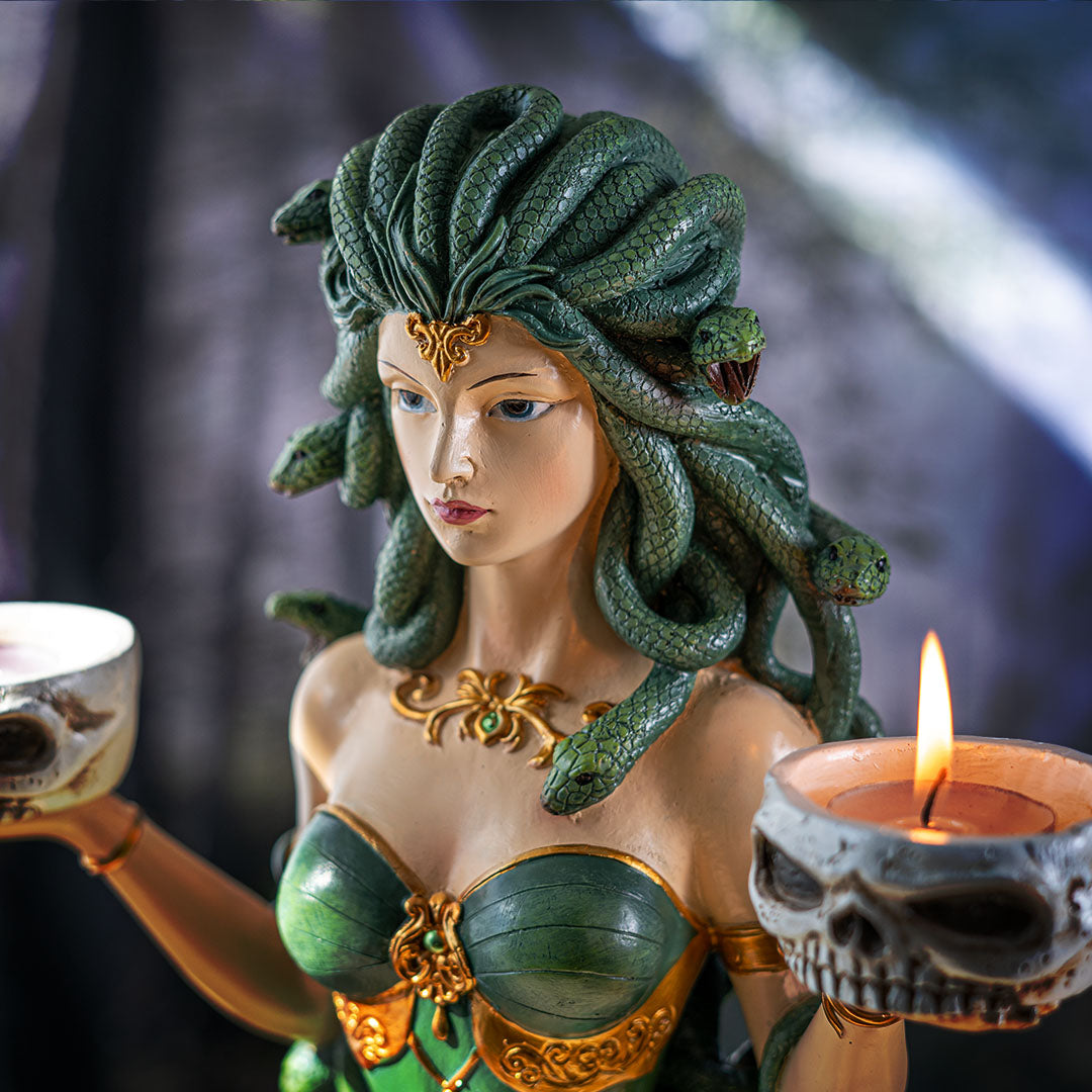 Closeup of green snake haired medusa figurine with skull bowls holding tealight candles