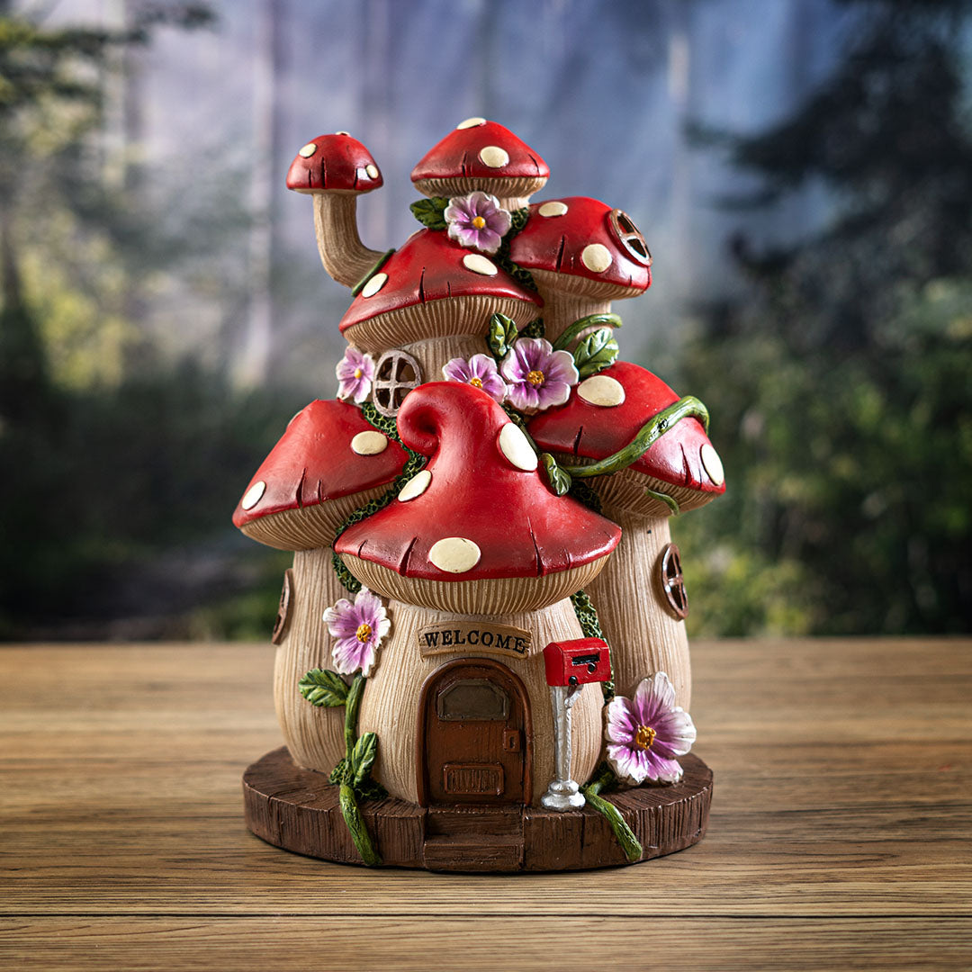 Figurine of a house made of mushrooms (red with white spotted caps) and pink flowers, door and welcome sign with mailbox