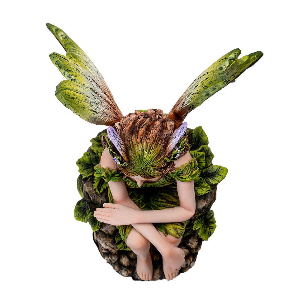 Figurine of pale fairy with brown hair, green dress and wings sitting amidst leaves, shown top down