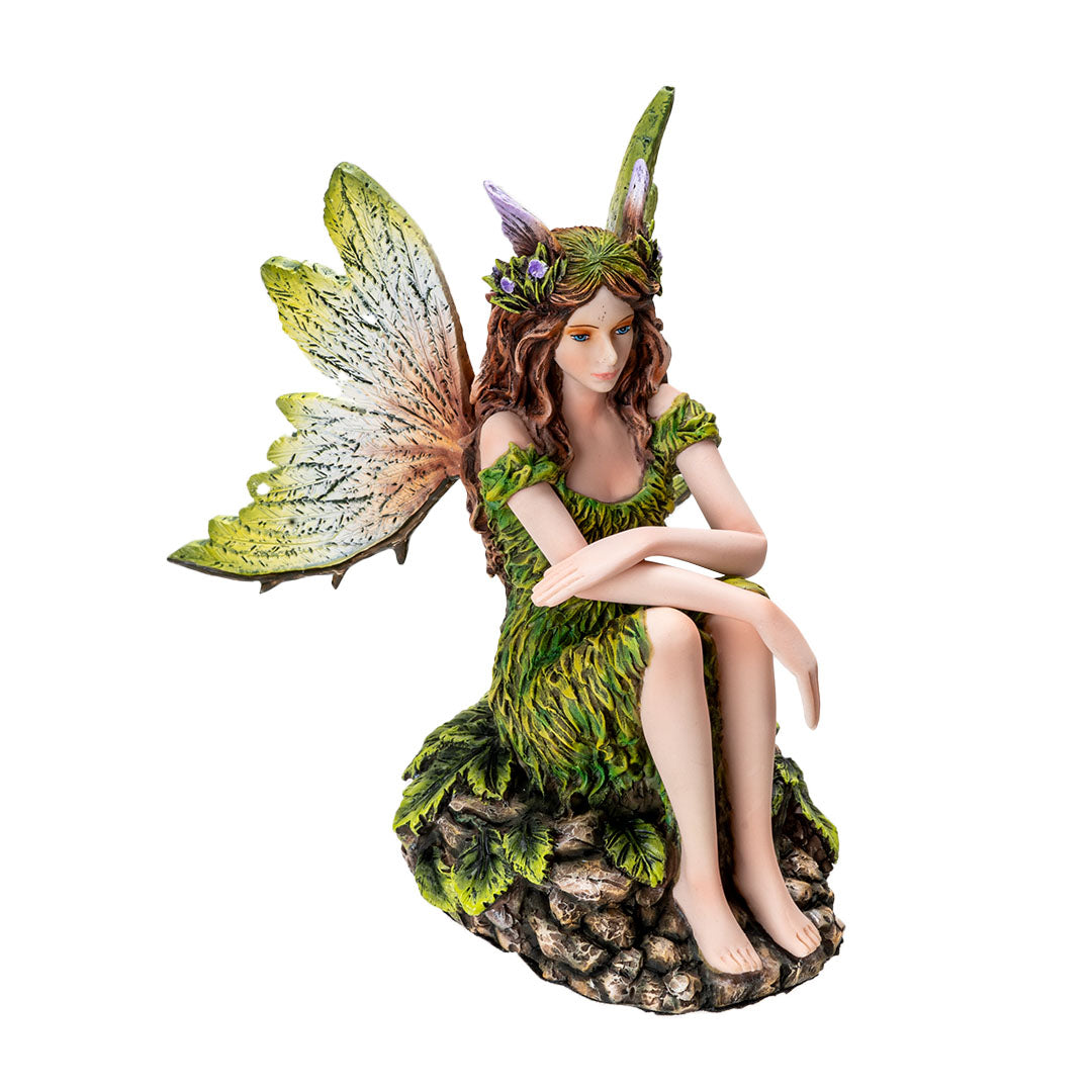 Figurine of pale fairy with brown hair, green dress and wings sitting amidst leaves