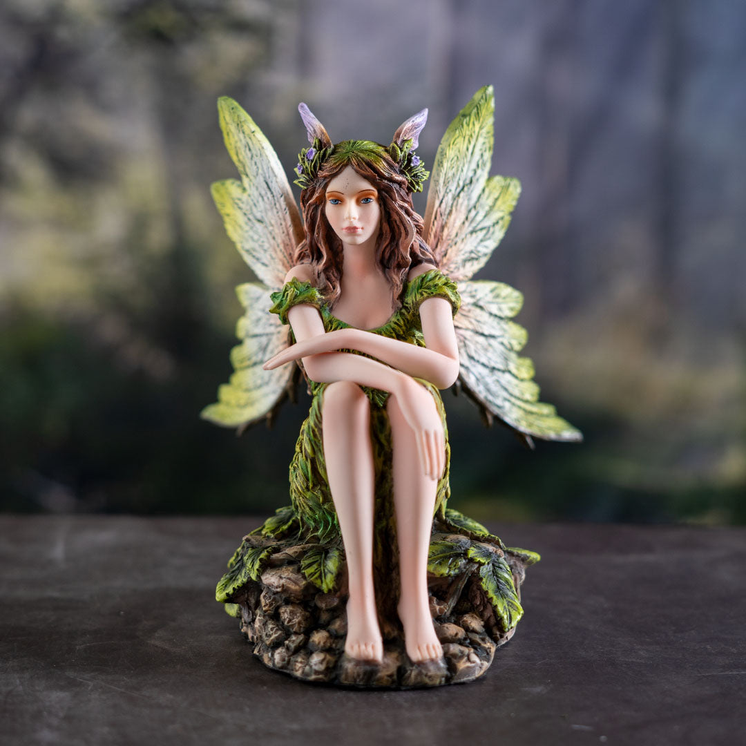 Figurine of pale fairy with brown hair, green dress and wings sitting amidst leaves