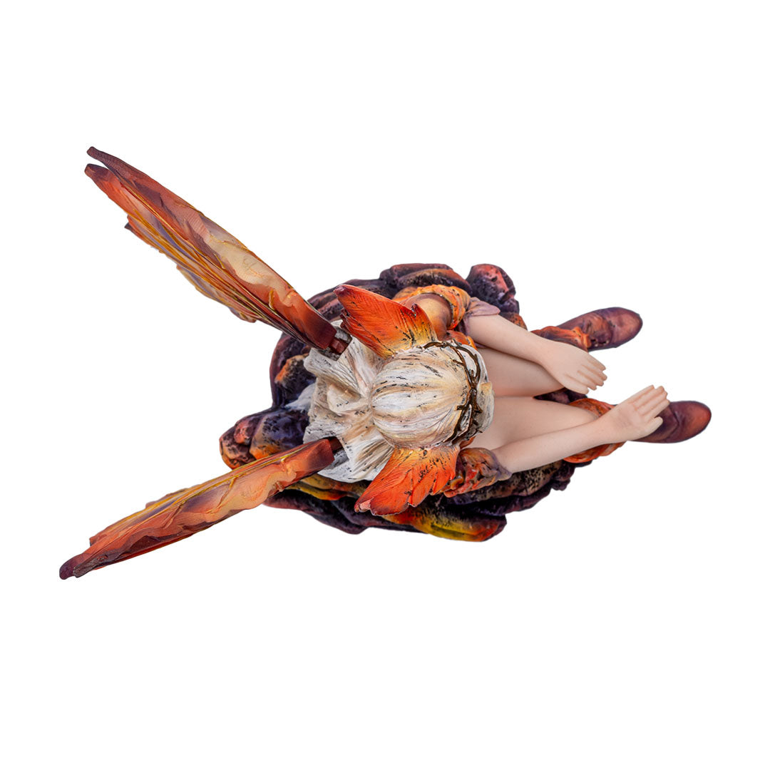 Figurine of blond fairy with orang wings and outfit sitting on a rock with her hand out, palm up, shown top down