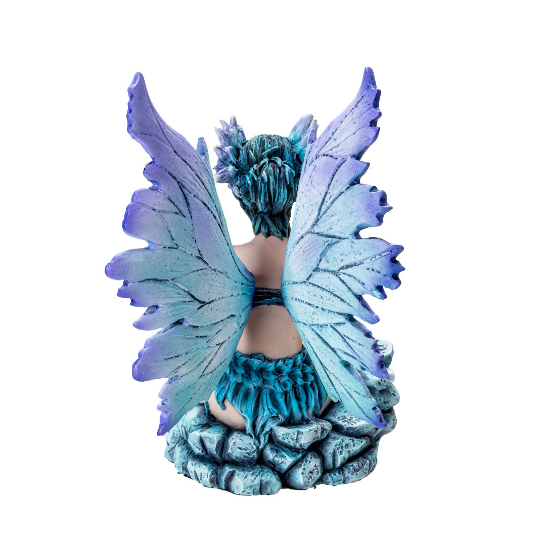 Figurine of a sitting fairy, blue-purple wings and green-blue hair, sitting on rocks with a butterfly, shown from the back