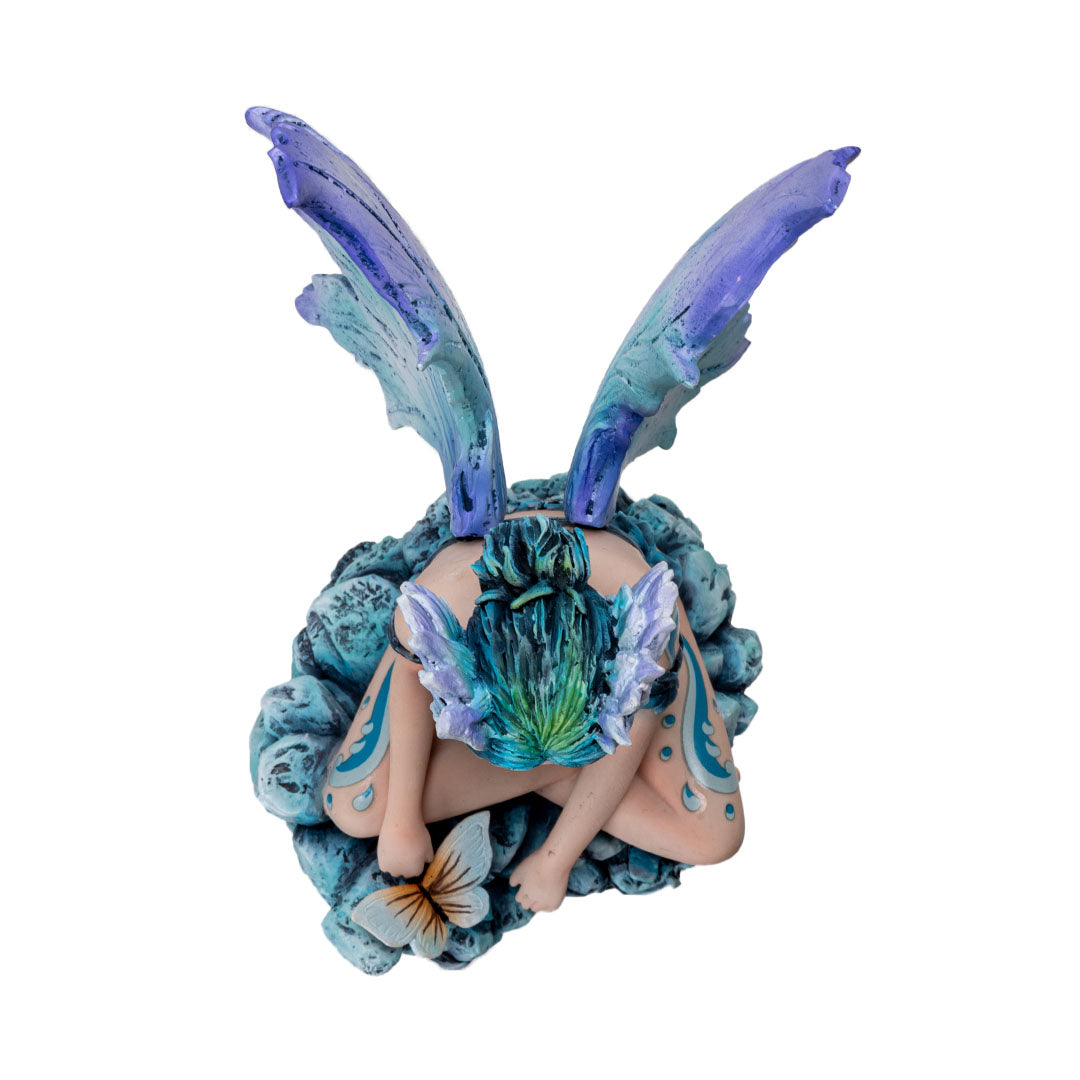Figurine of a sitting fairy, blue-purple wings and green-blue hair, sitting on rocks with a butterfly, shown top down