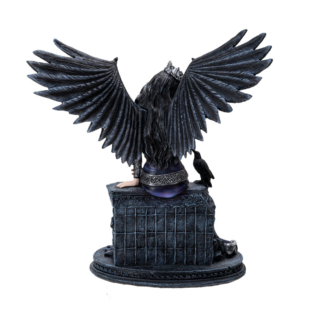Fairy figurine, black feathered wings and hair, she wears a crown, pale skin, black and blue dress, sitting on a wall with a raven. shown from the back