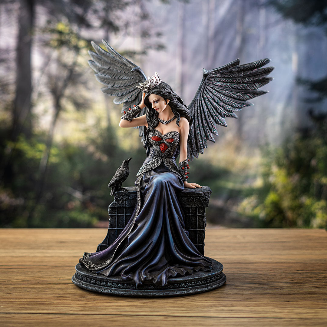Fairy figurine, black feathered wings and hair, she wears a crown, pale skin, black and blue dress, sitting on a wall with a raven