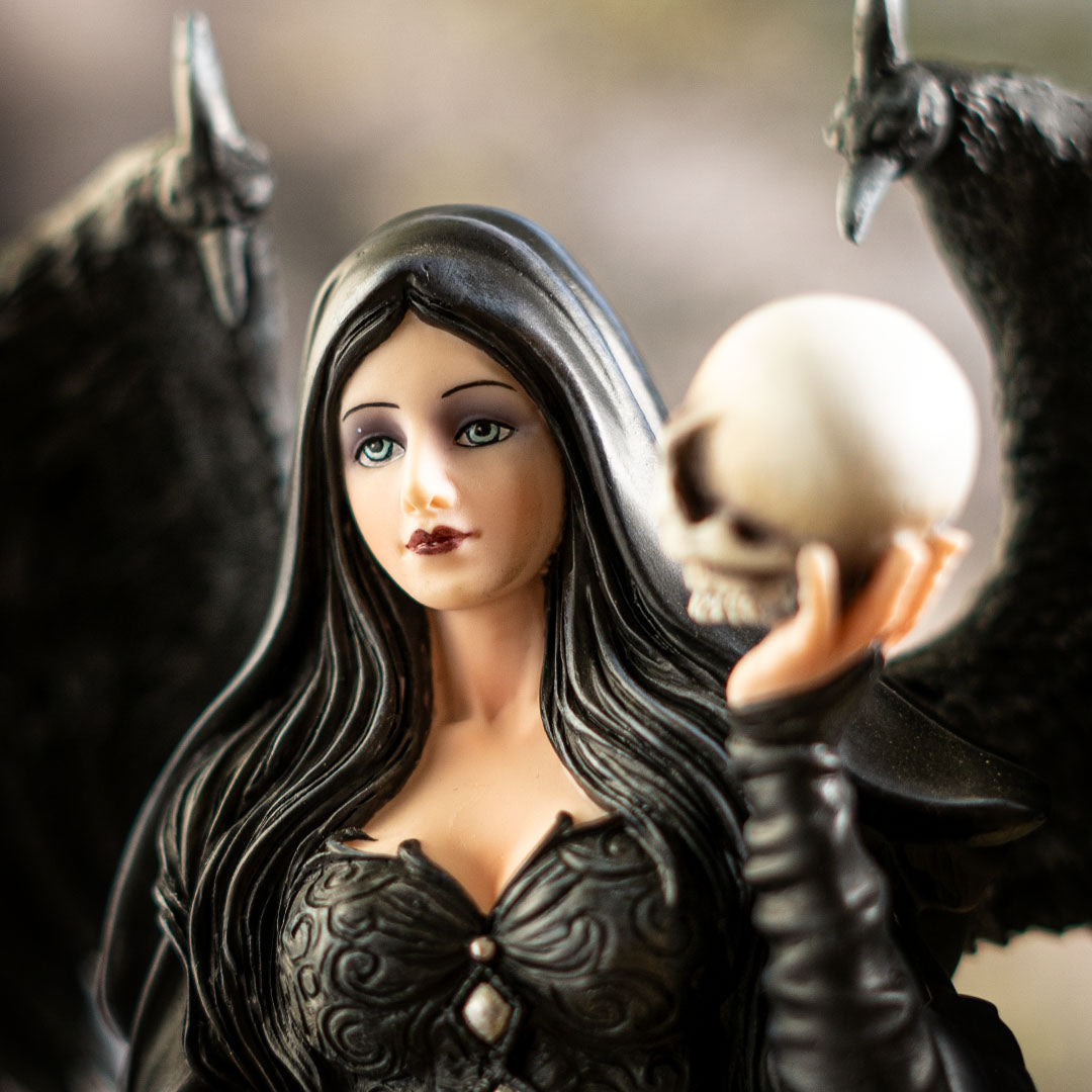 Closeup of blue eyed woman in black cloak, ebony hair, holding a skull