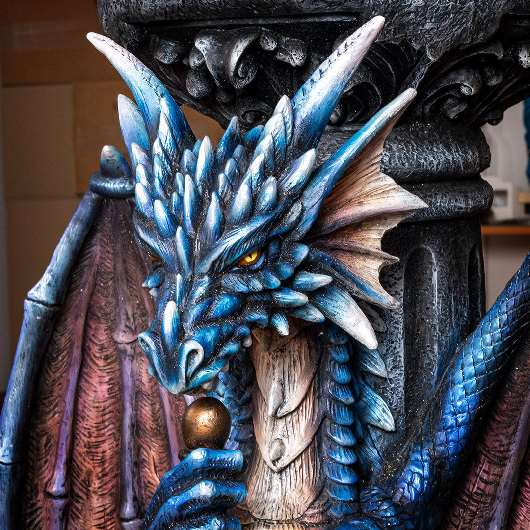 Close up of blue dragon with detailed scales, yellow eyes, gold topped sword, red-purple accents on wings