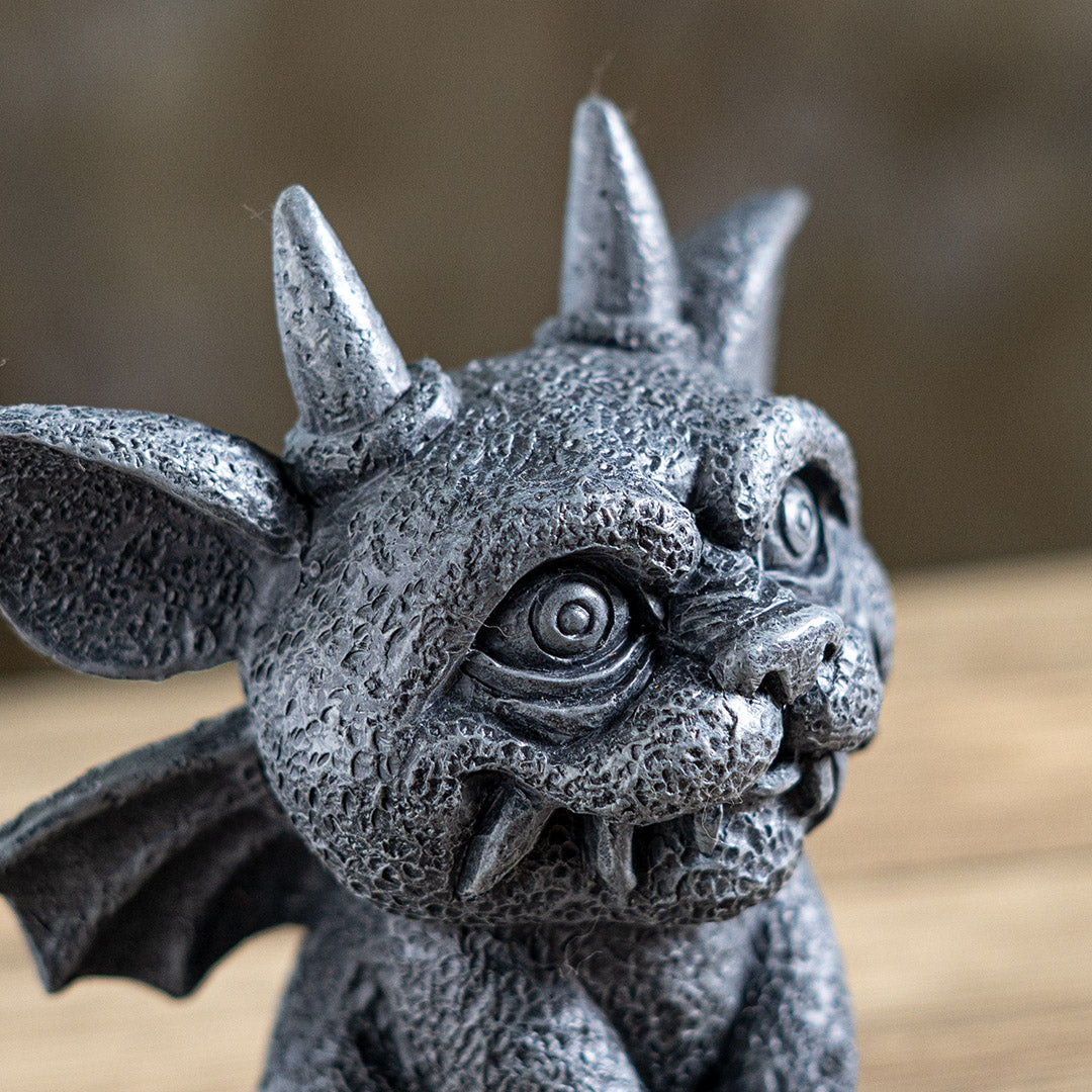 Statue of a gargoyle creature with large eyes, horns and wings in faux-stone finish, close up of grinning face