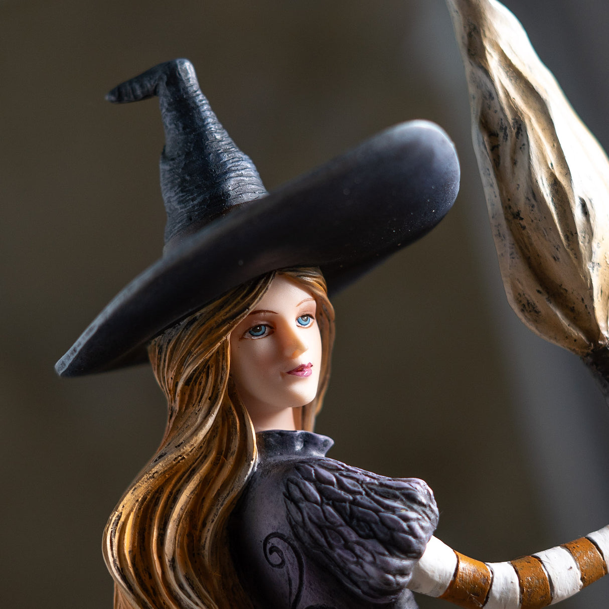 Closeup of witch holding broom, blond hair, blue eyes, black hat