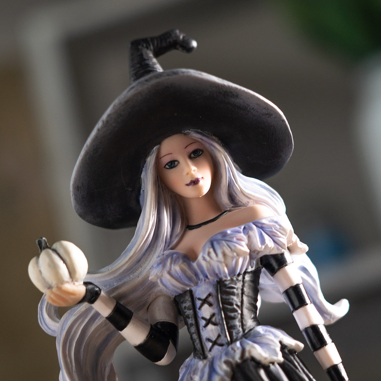 Closeup of witch figurine in white and black, white hair, holding pale pumpkin