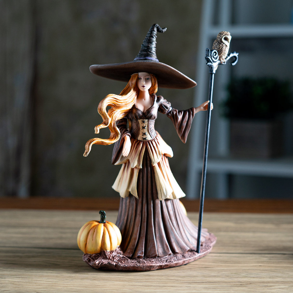 Figurine of witch with red hair, brown dress, surrounded by pumpkins, owl perched on her staff