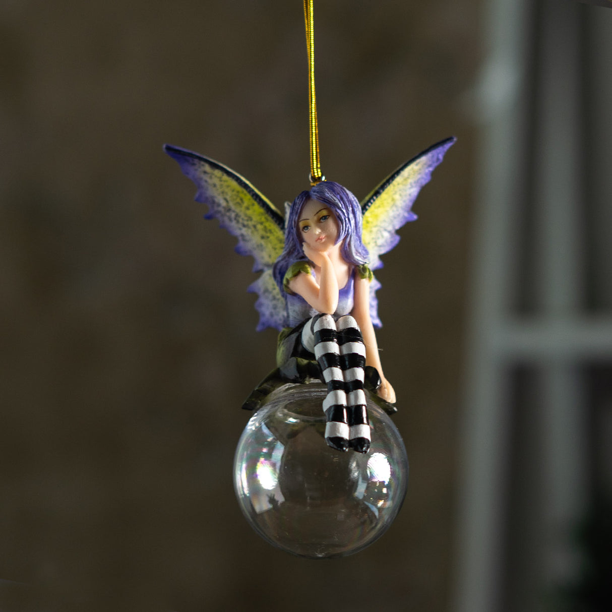 Fairy ornament with purple hair and striped pants sitting on a clear glass ball. Purple and yellow wings, gazing out