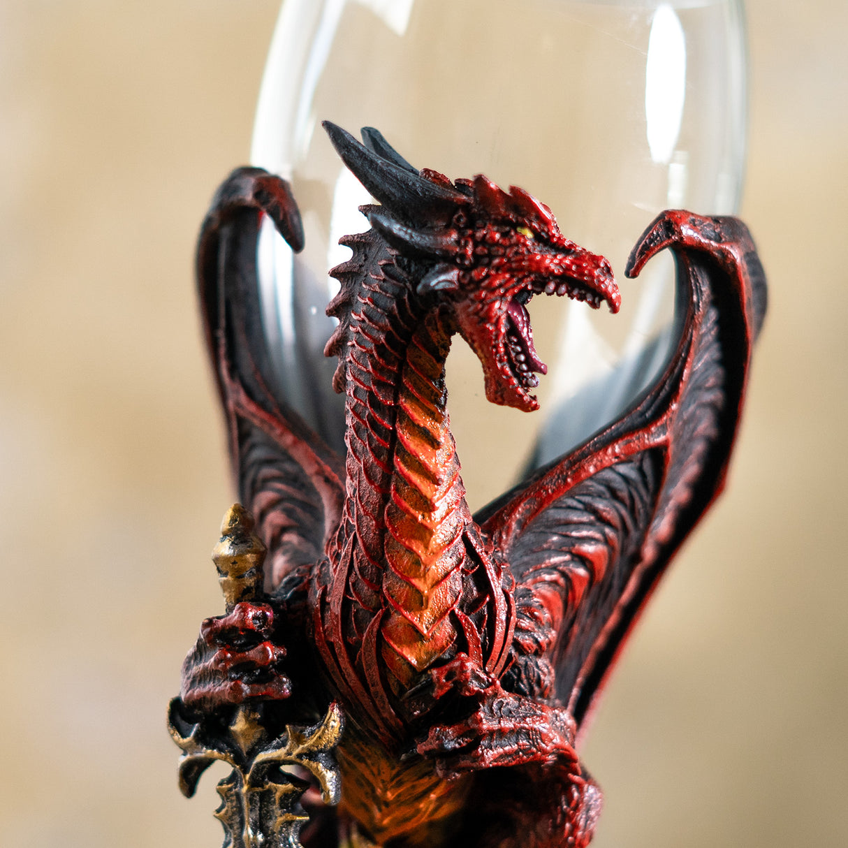 Closeup of red dragon, yellow eye, orange and black accents, holding a sword with gold hilt, glass goblet