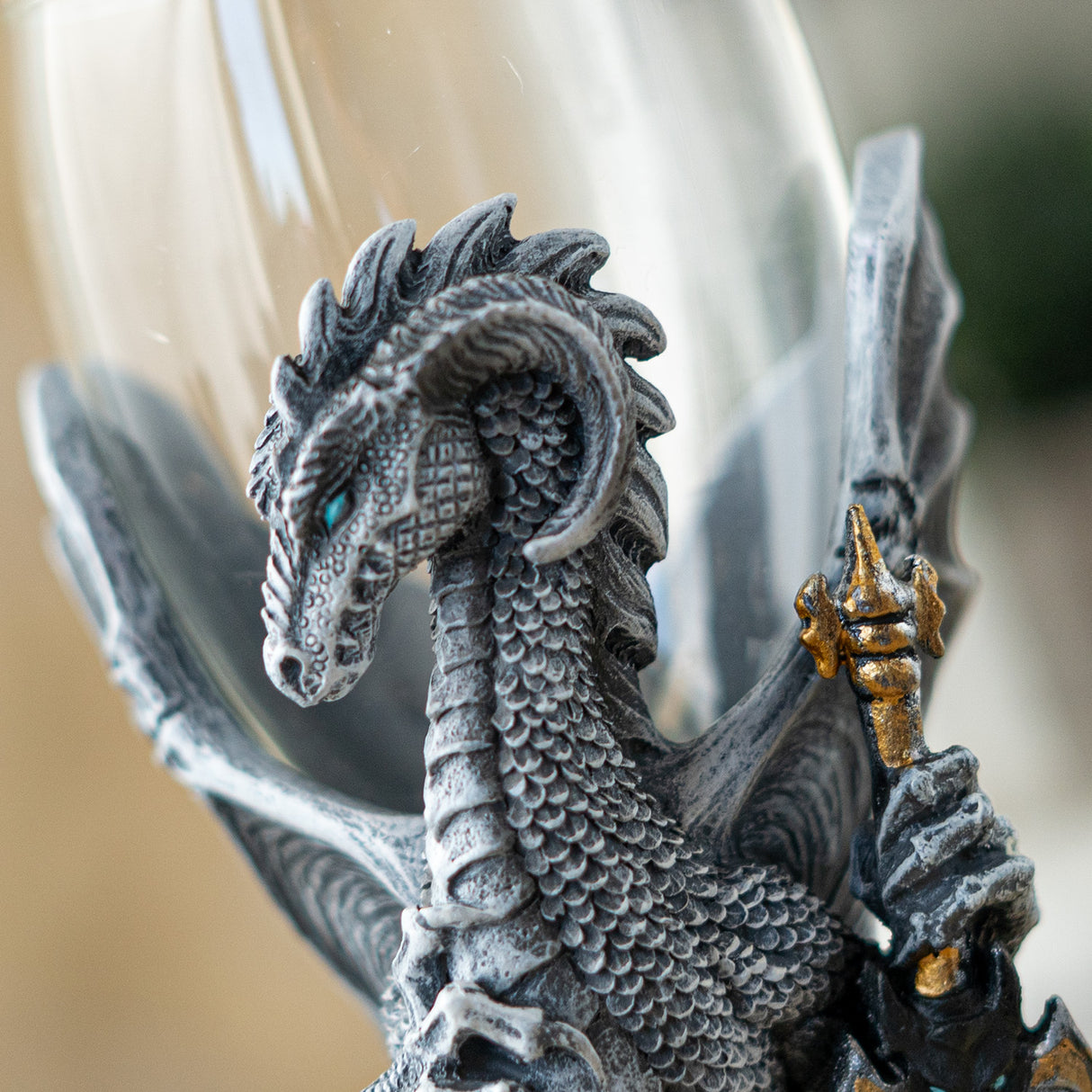Closeup of gray dragon, blue eye, gold hilt of sword, glass goblet