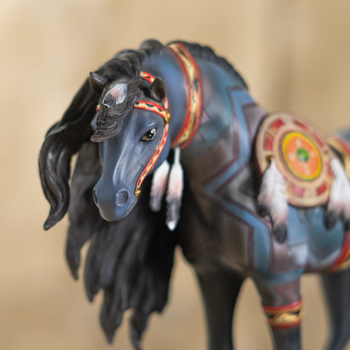 Closeup of horse figurine, blue-gray with black mane, red and gold accessories and feathers