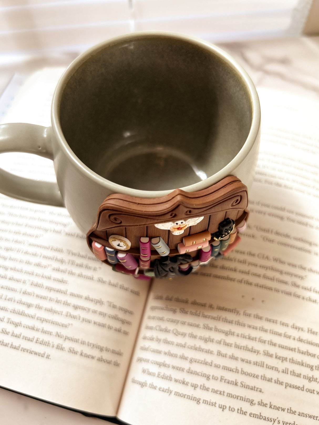 Decorative bookshelf mug with miniature books and items shown on an open book