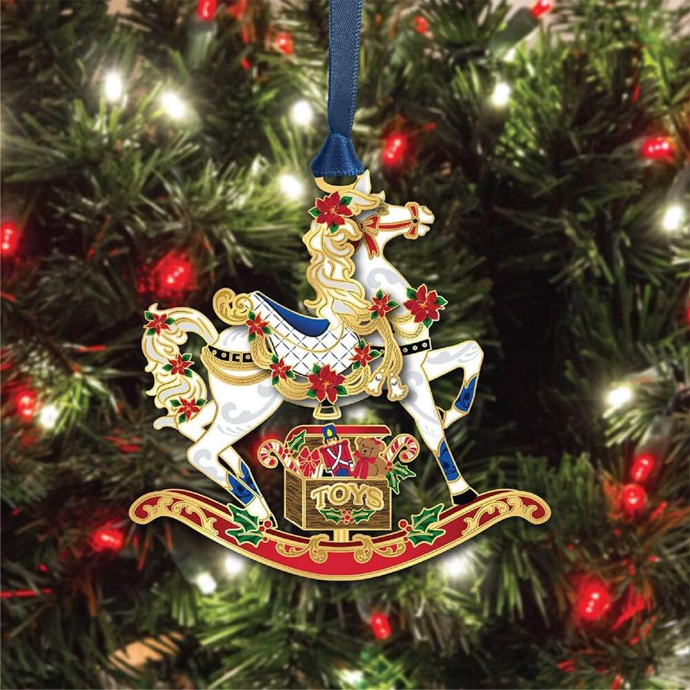 Brass rocking horse ornament with a box of toys, accented in holly and poinsettia, shown on a tree