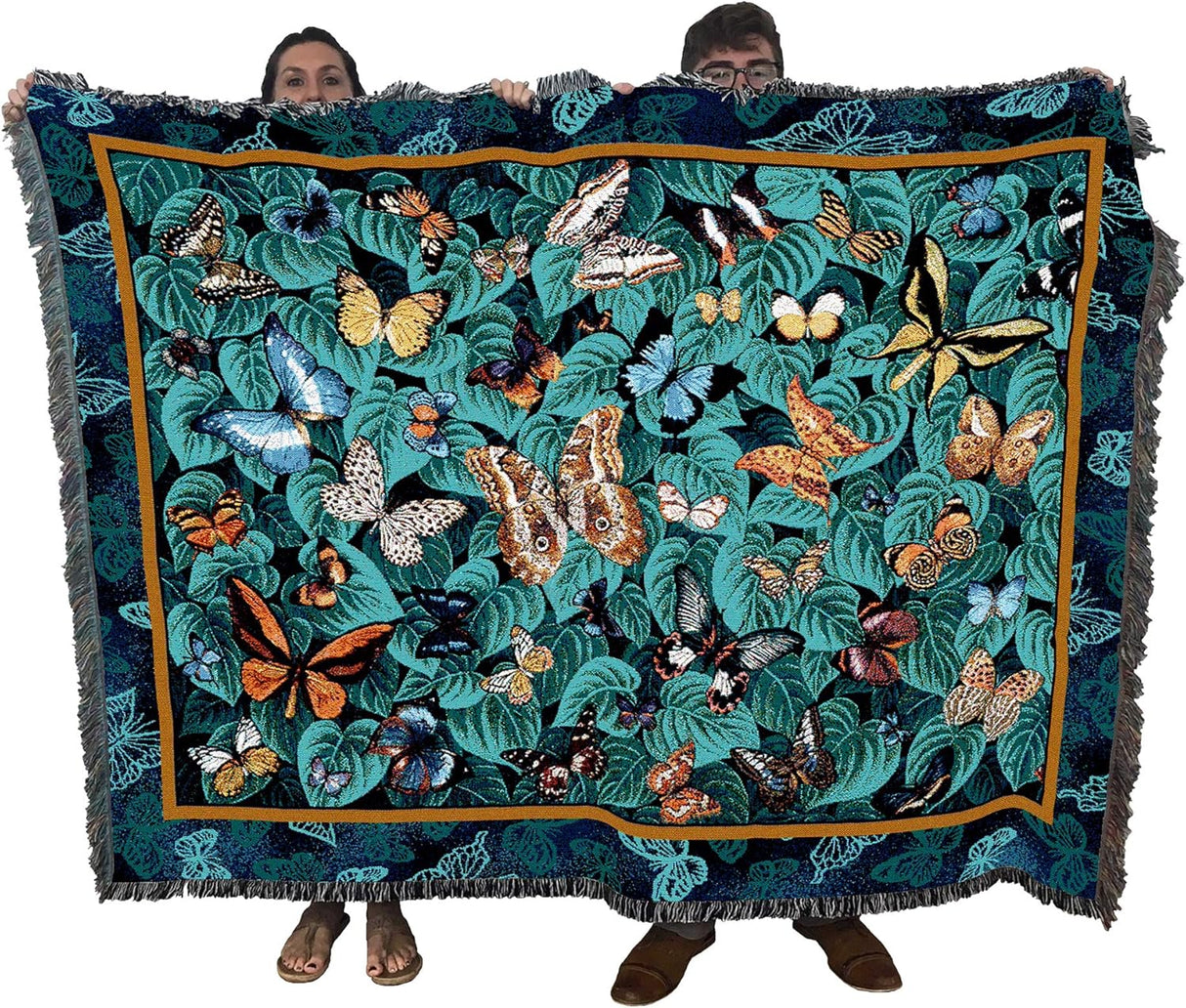 Woven tapestry blanket featuring various butterflies on a green-teal leaf background, held up by two adults to show large size