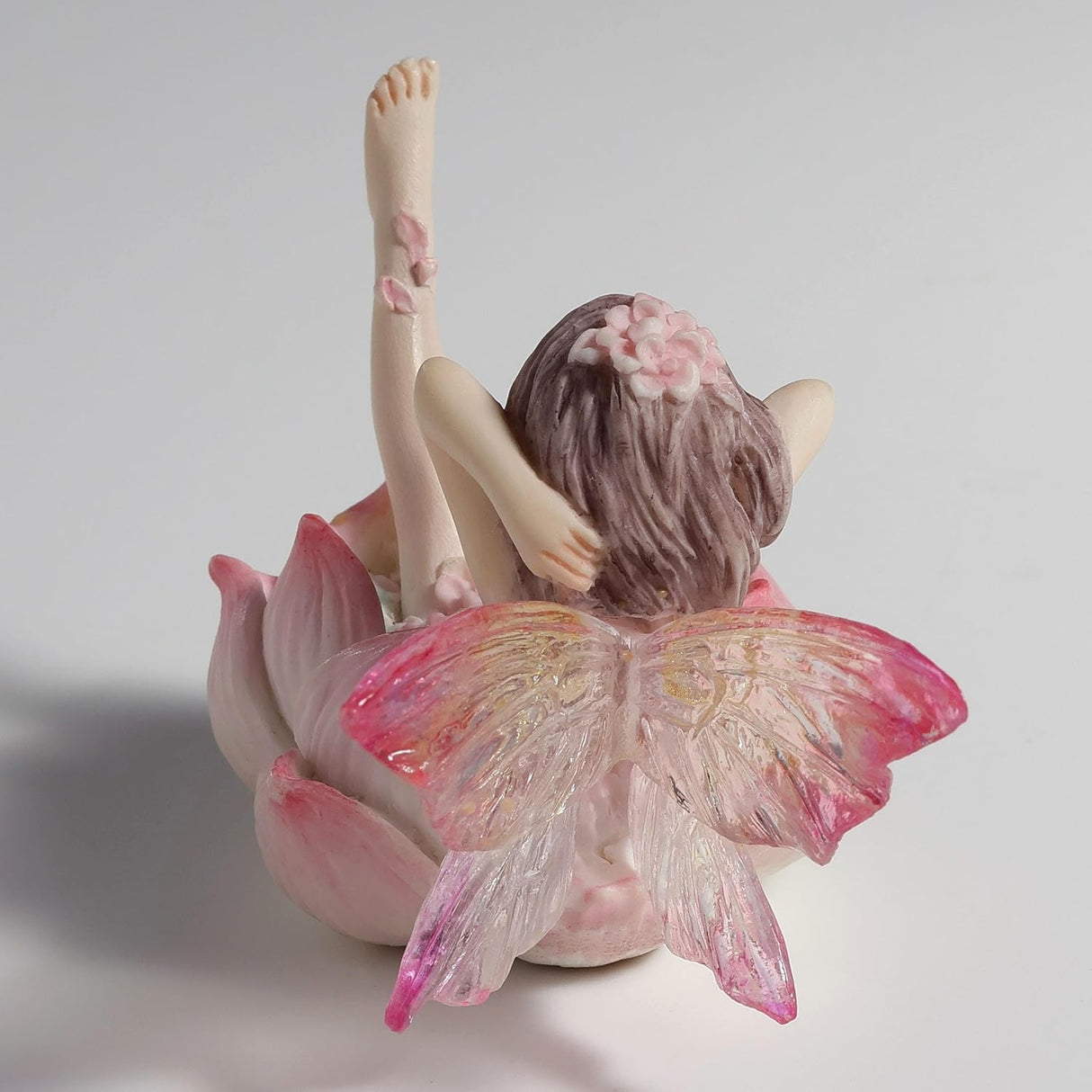 Figurine of a fairy with transparent wings in pink and clear reclining in a flower to have a bath, covered in pink petals