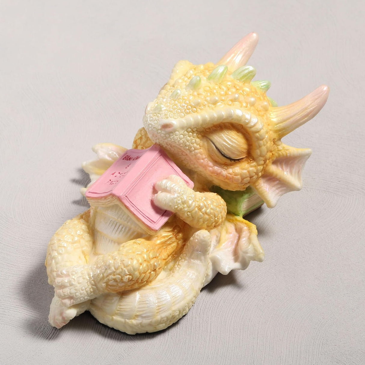 Cute sleeping dragon figurine holding a pink book