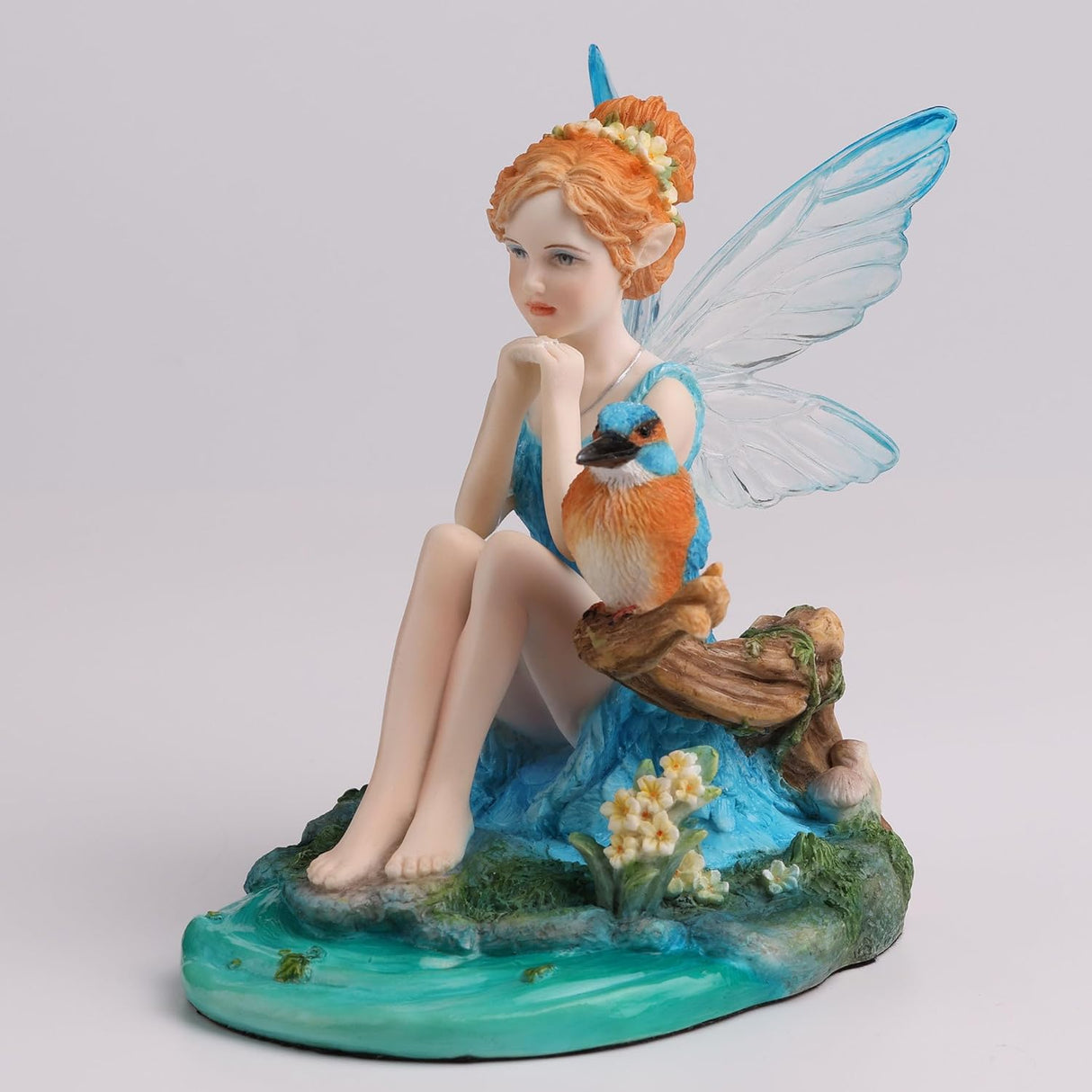 Figurine of fairy in blue dress with matching wings and red hair sitting by pond with kingfisher bird