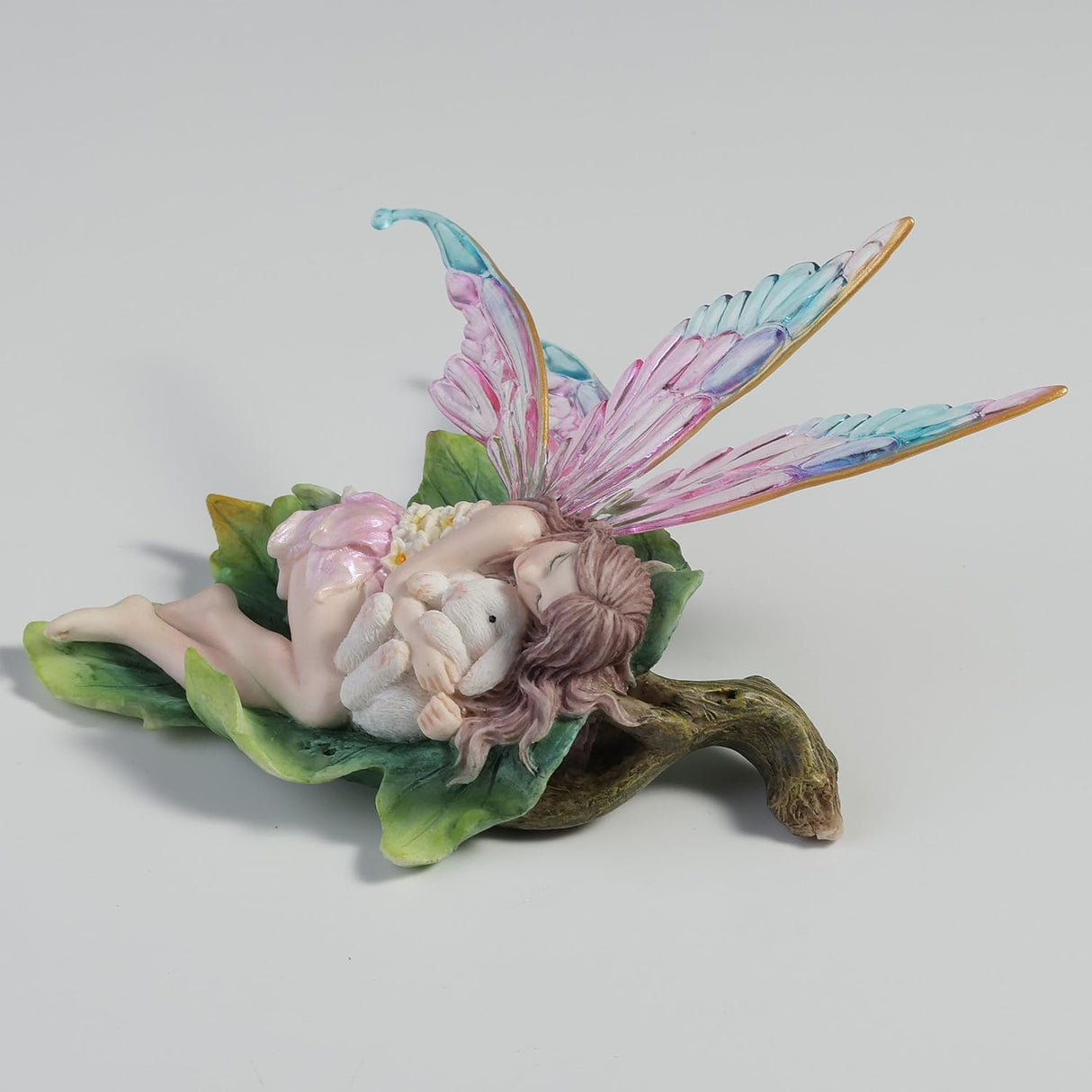 Fairy figurine with colorful wings, cuddling a bunny on a leaf