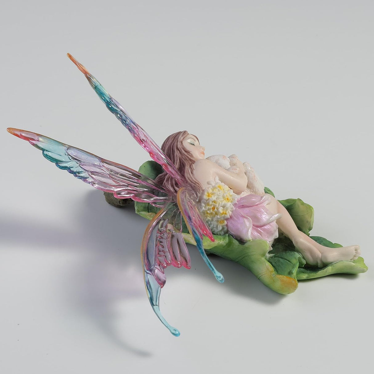 Fairy figurine with colorful wings, cuddling a bunny on a leaf
