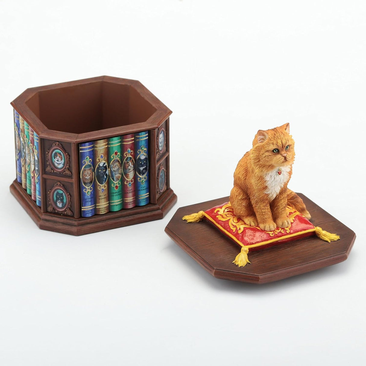 Trinket box of orange cat sitting on a red and yellow pillow on the lid of a faux-wood box shaped like a bookshelf with cat books and pictures. Shown from the back