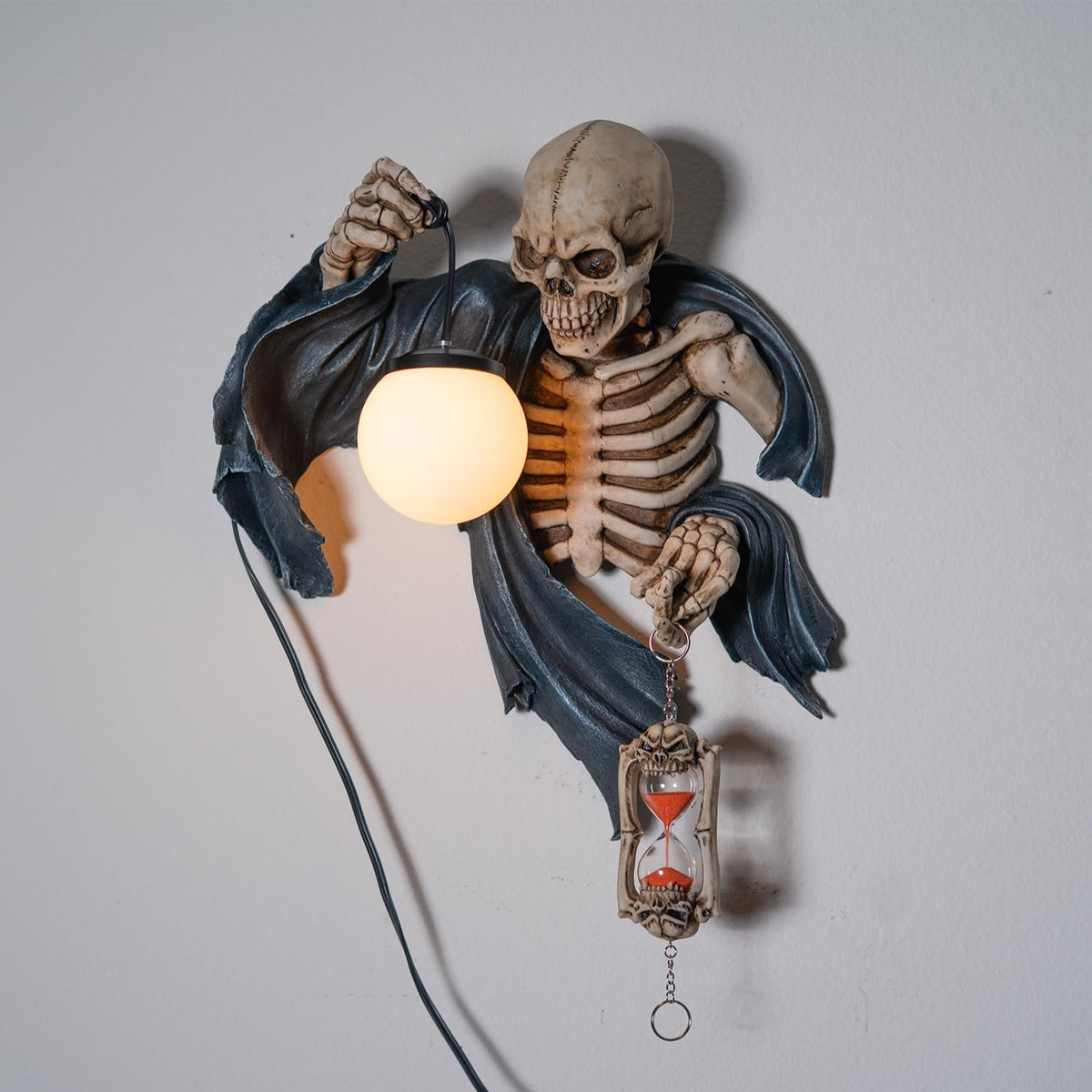 A wall lamp featuring a skeleton in black torn robe holding an orb light in one hand, hourglass in the other