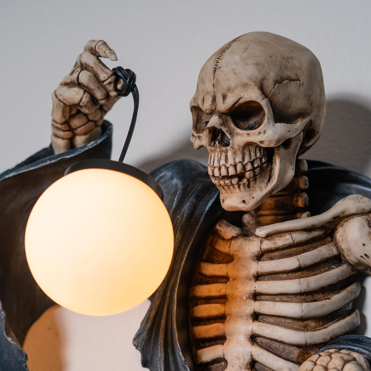 A wall lamp featuring a skeleton in black torn robe holding an orb light in one hand, hourglass in the other