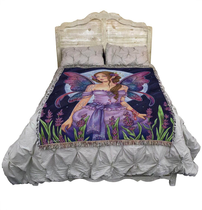 Tapestry blanket with art by Brigid Ashwood. Fairy in purple dress with purple-blue wings standing in a flower field with full moon beyond.  Shown on a bed.