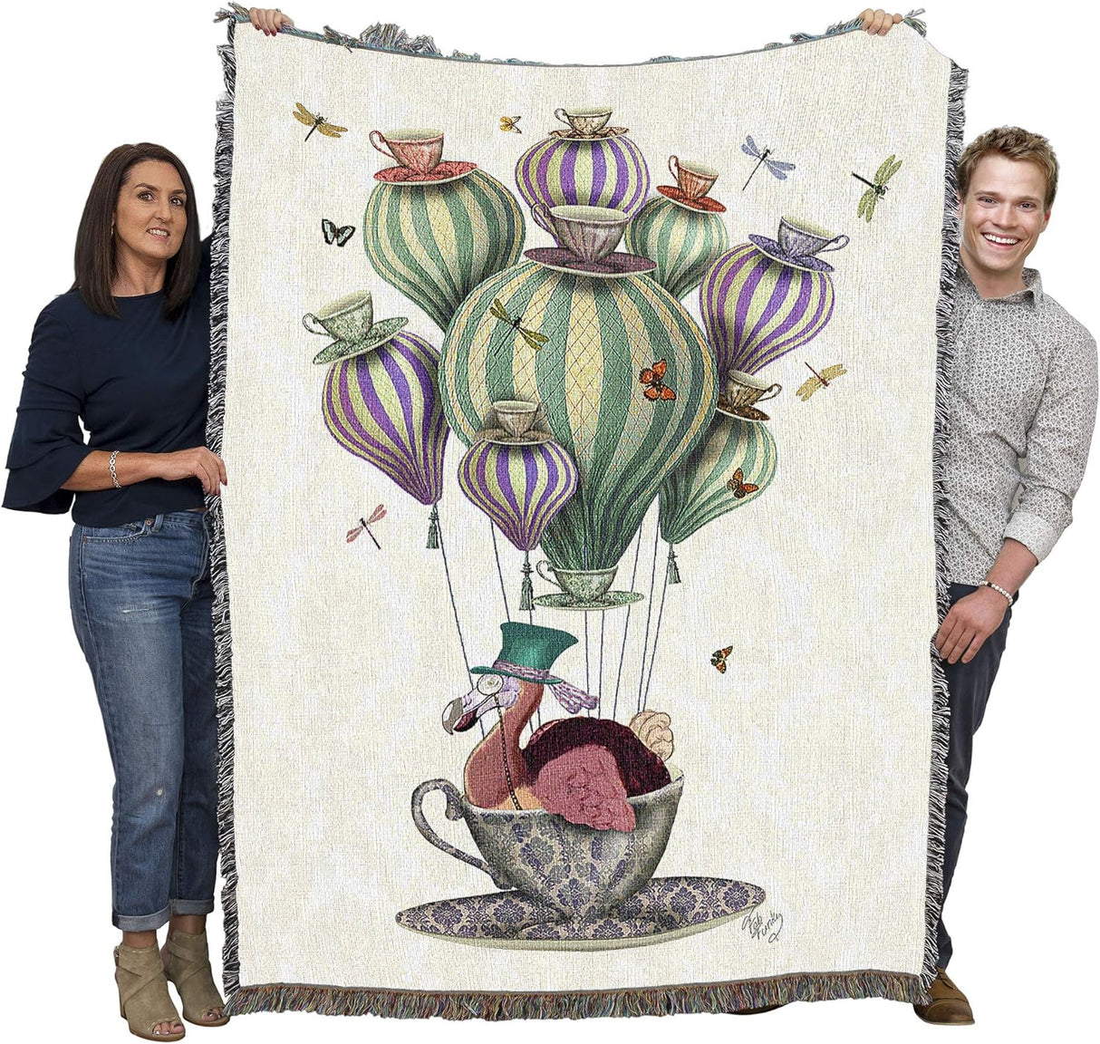 Woven blanket with a colorful design of a dodo in a teacup on hair balloon with dragonflies and butterflies, held up by two adults