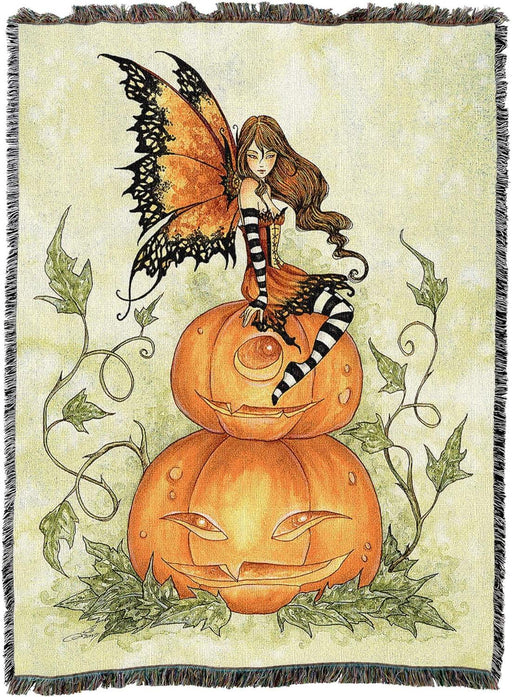 Tapestry blanket with a fairy in orange perched upon two stacked jack-o-lantern pumpkins