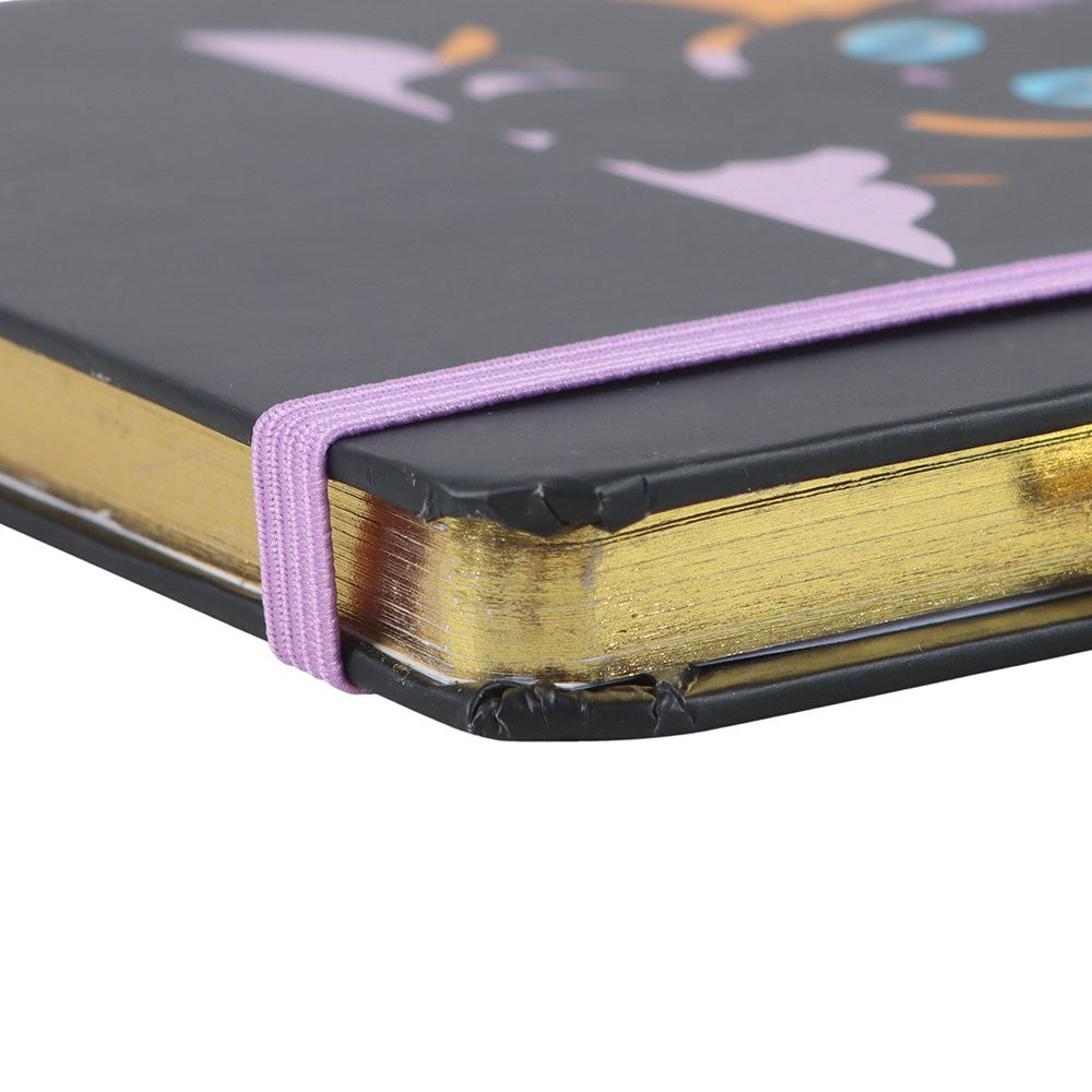 Close-up of a notebook with a black cover, gold binding, and purple elastic band.